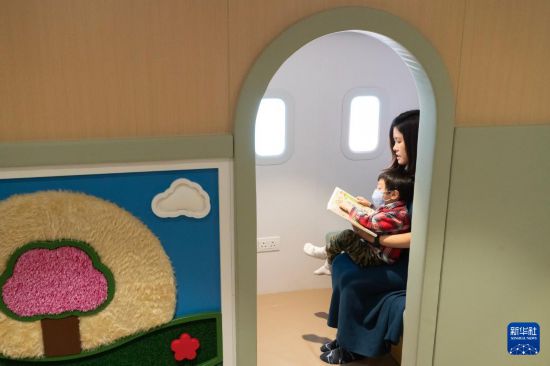 　　在位于香港国际机场一号客运大楼的“感知阁”内，邓女士陪伴被诊断为孤独症的儿子阅读搭乘飞机的绘本（3月31日摄）。 新华社发（龙镜伊 摄）